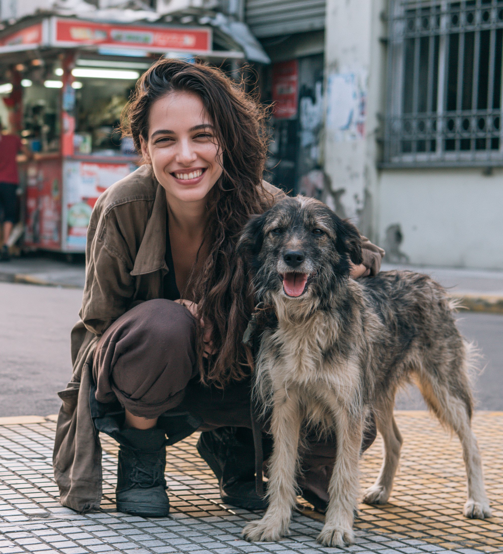 Paseadora sonriendo, agachada junto a un perro mestizo en una vereda de Buenos Aires